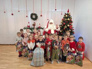 Dzieci z grupy IV pozują do zdjęcia ze Świętym Mikołajem i prezentami.