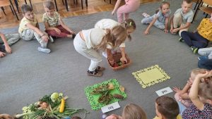 Dwie dziewczynki wkładają do koszyka dary lasu: liście i kasztany.