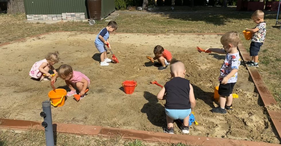 Grupa dzieci z oddziału III bawi się w piaskownicy - nasypują piasek do wiaderek, kopią, grabią.