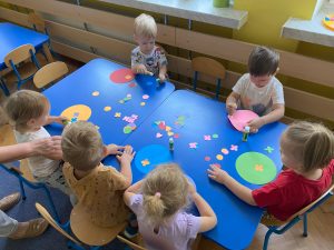 Przedszkolaki przyklejają ozdoby na swoich piłeczkach powycinanych z kolorowego papieru