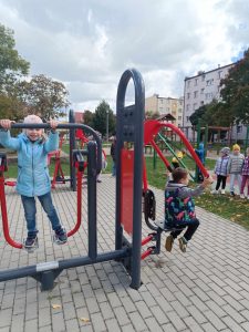 Dwoje dzieci pozuje do zdjęcia na siłowni plenerowej. Ćwiczą nogi i ramiona.