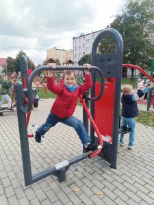 Chłopiec pozuje do zdjęcia na przyrządzie z siłowni plenerowej. Pokazuje jak ćwiczyć nogi.