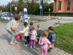 Nauczycielka przed przejściem dla pieszych tłumaczy dzieciom zasady bezpiecznego przechodzenia przez jezdnię