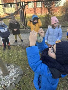 Chłopiec zawiesza smakołyki dla ptaków na gałęzi drzewka.