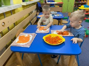 dwóch chłopców przy stoliku wykleja pomarańczową  włóczką ogonek wiewiórki