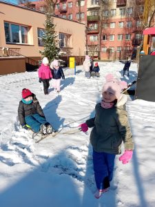 Dzieci bawią się na śniegu - rzucają śnieżkami, wożą na sankach.