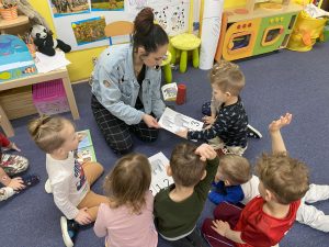 przedszkolaki siedząc na dywanie wraz z nauczycielką przeliczają na obrazkach słonie