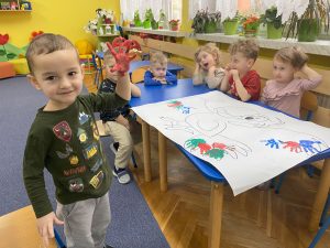 Dzieci odbijają dłonie pomalowaną farbą na ogromnej kolorowance papugi.