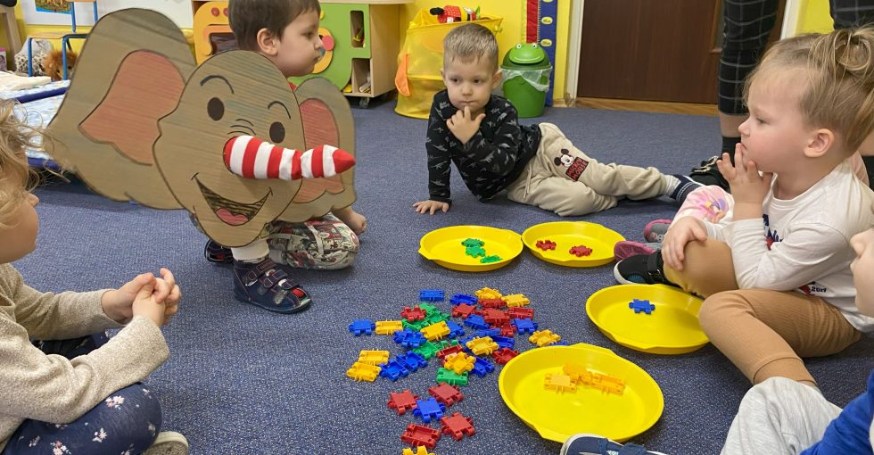 Dziecko segreguje kolorowe klocki ręką ubraną w skarpetę, imitującą trąbę słonia.